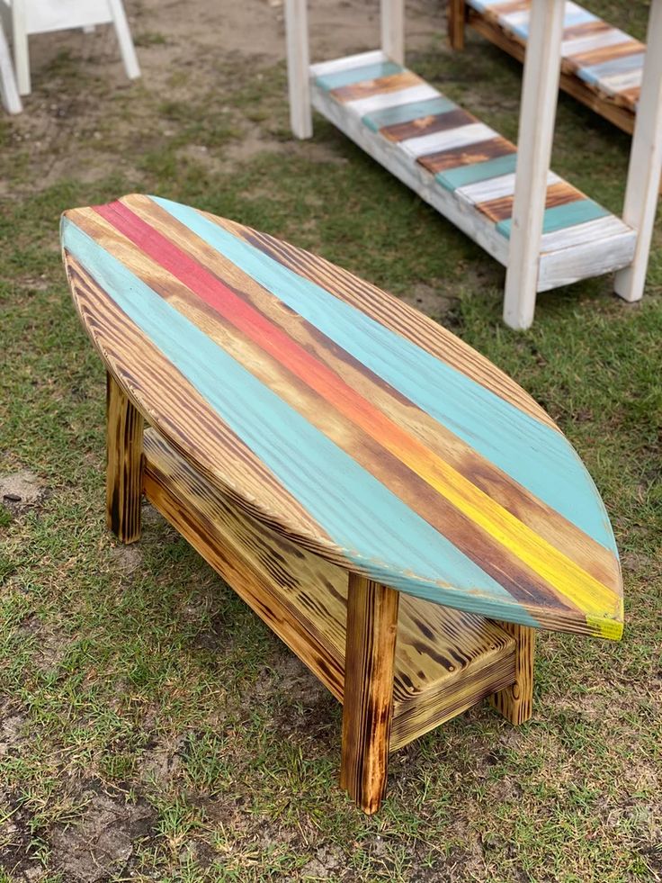 a surfboard shaped table sitting on top of grass next to white chairs and tables