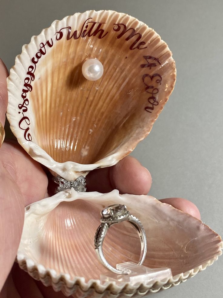 a person holding two seashells with a wedding ring in it's shell