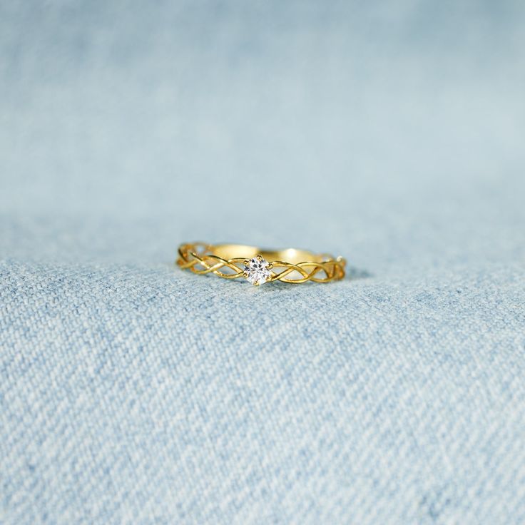 a yellow gold ring with a single diamond on the middle, sitting on a blue cloth