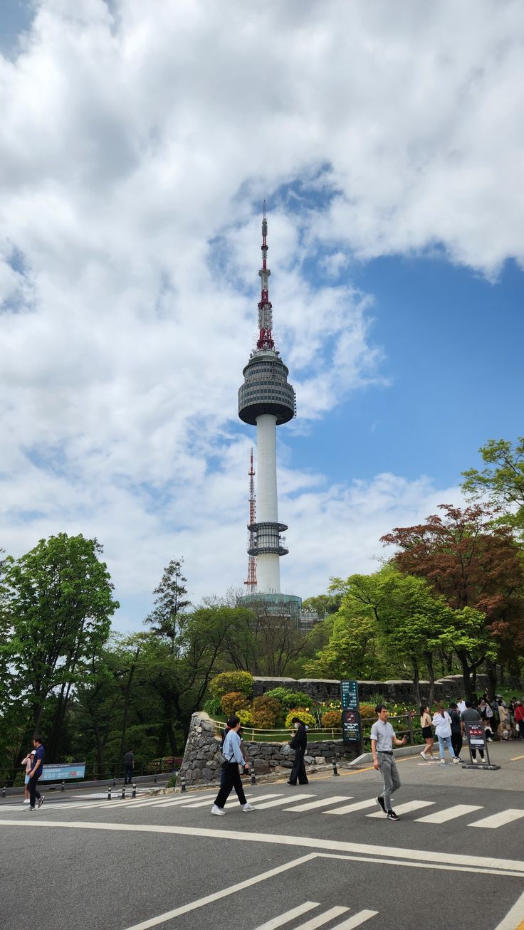 people crossing the street in front of a tall building with a tv tower on top