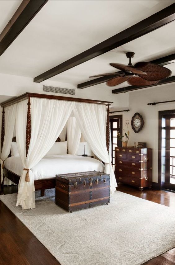 a bedroom with a canopy bed and white drapes on the ceiling, along with an antique trunk