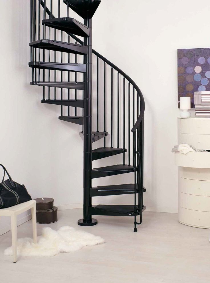 a spiral staircase in a white room with black railing and handbag on the floor