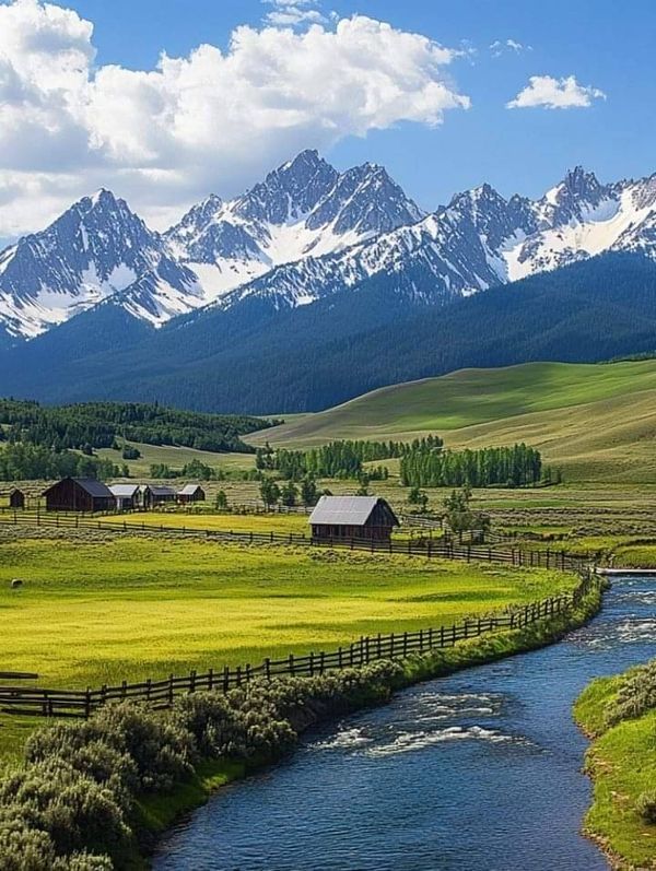 a river running through a lush green field with mountains in the backgrouund