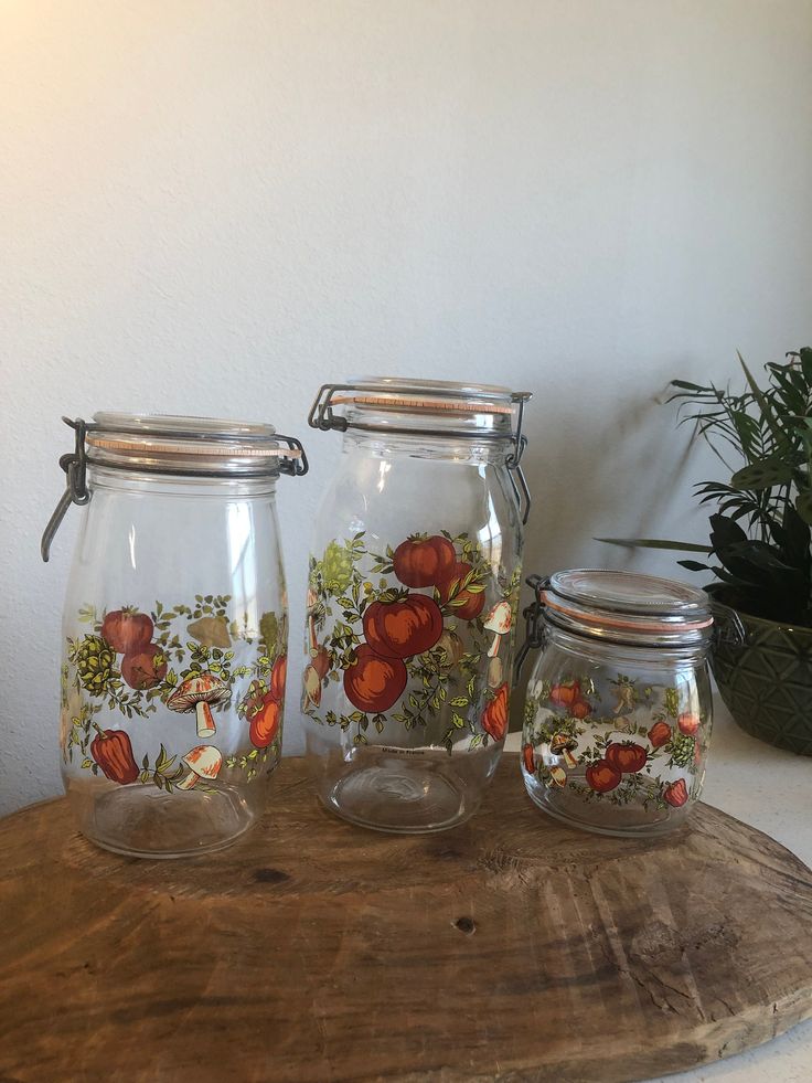 three glass jars with flowers painted on them sitting on a wooden table next to a potted plant