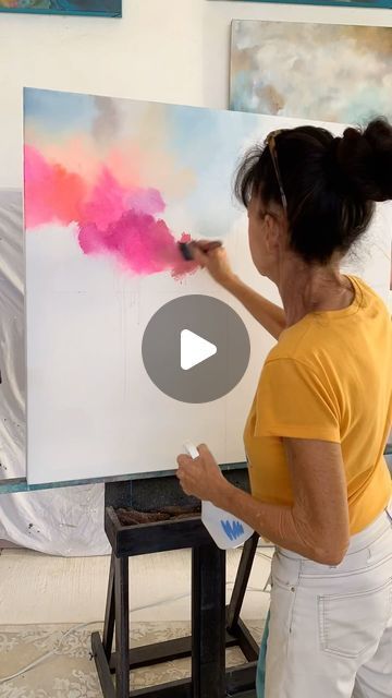 a woman is painting on an easel with pink and red colors in the background