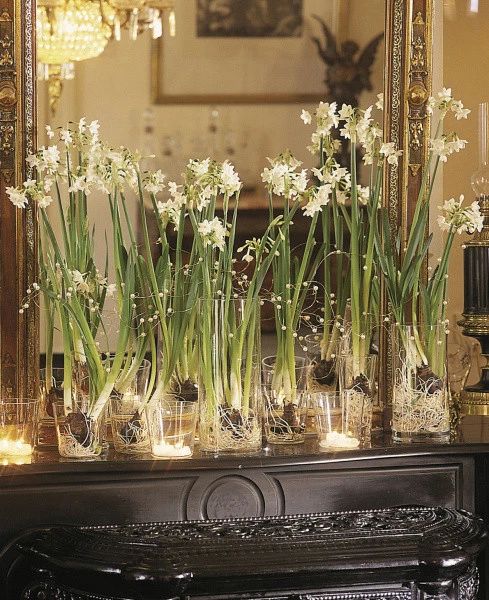 flowers are in vases sitting on a mantle with candles and a mirror behind them