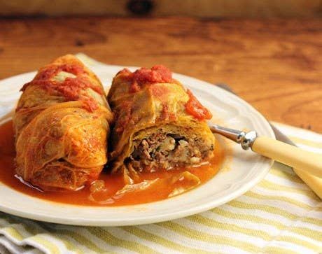 a white plate topped with stuffed cabbage rolls covered in tomato sauce and marinated meat