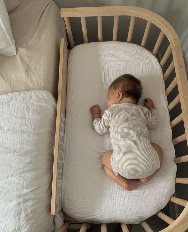 a baby laying in a crib on top of a white sheet covered bed next to pillows