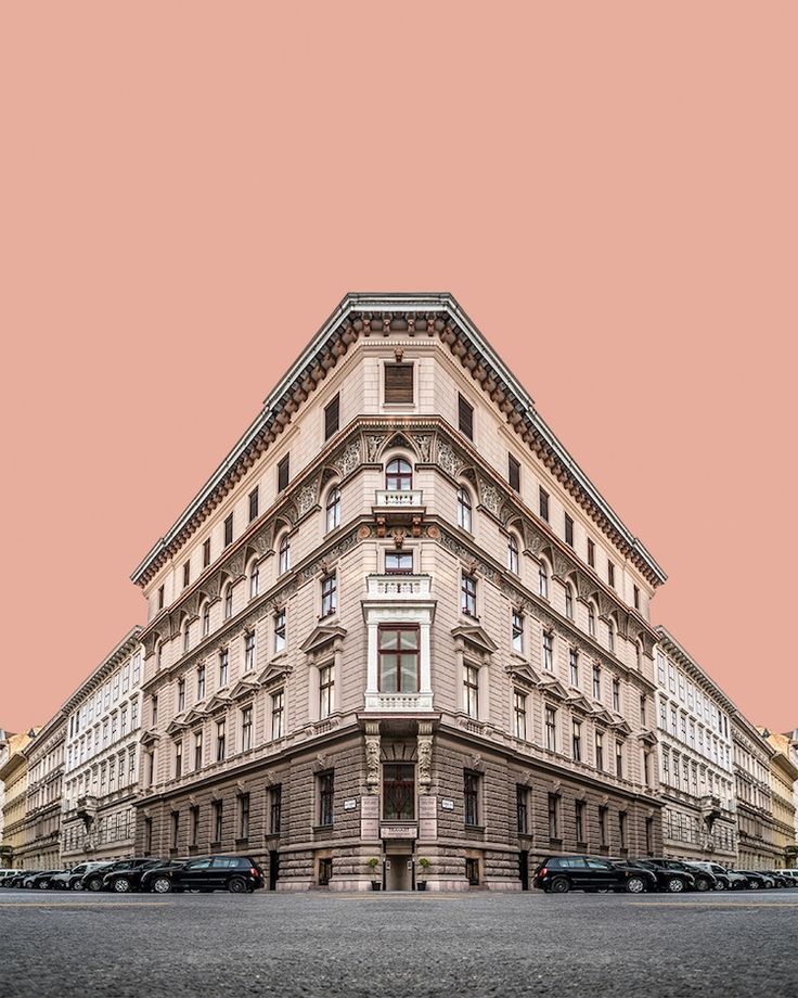 an old building with cars parked on the street in front of it and a pink sky