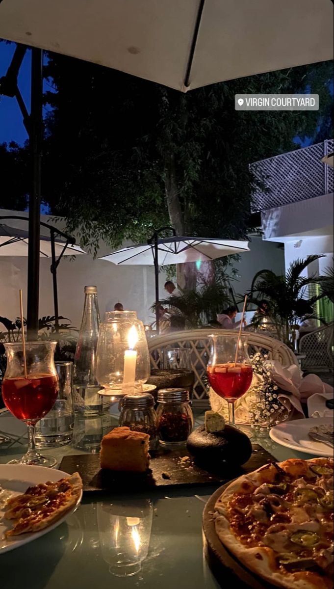 a table with pizzas and glasses of wine on it at an outdoor dining area