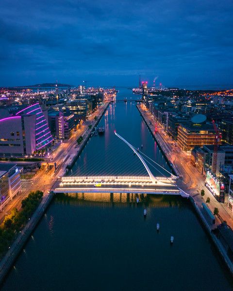 an aerial view of a city at night with the lights on and bridge in the foreground