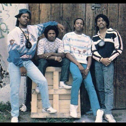 four young men posing for a photo in front of a wooden door with graffiti on it