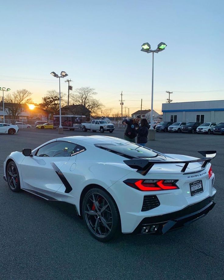 a white sports car parked in a parking lot with the sun shining down on it