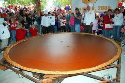 a group of people standing around a large wooden table in front of a wall with an advertisement on it