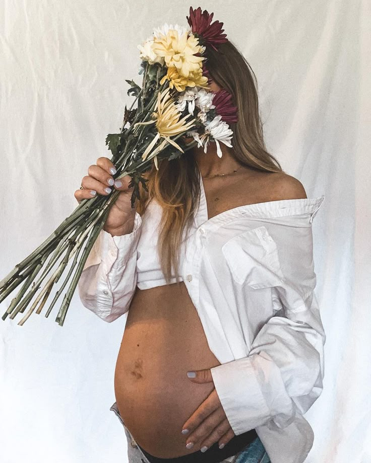 a pregnant woman with flowers in her hair is wearing a white shirt and denim jeans