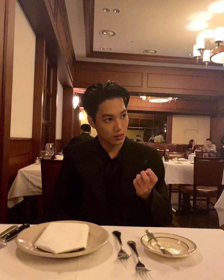 a young man sitting at a table in front of a plate with silverware on it