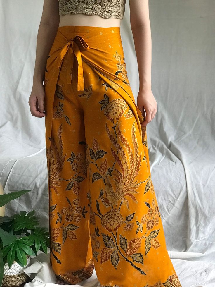 Gold Batik Wrap Pants *DETAILS* -These batik wrap pants are made of super-soft cotton fabric in a relaxed fit, very breathable, comfortable, and stylish to wear. -The unique bird and floral motif was naturally hand-drawn by small artisans here in Bali. -This wide leg pants have high slit at the side it creates beautiful flows when you move. -There is also adjustable tie belt in the waistline both in the front and in the back to fit your body.  This boho pants are perfect for any occasion such as Bali Beach, Rainbow Skirt, Pants Boho, Bali Beaches, Festival Pants, Wrap Pants, Slow Fashion Brands, Boho Pants, Flowy Pants