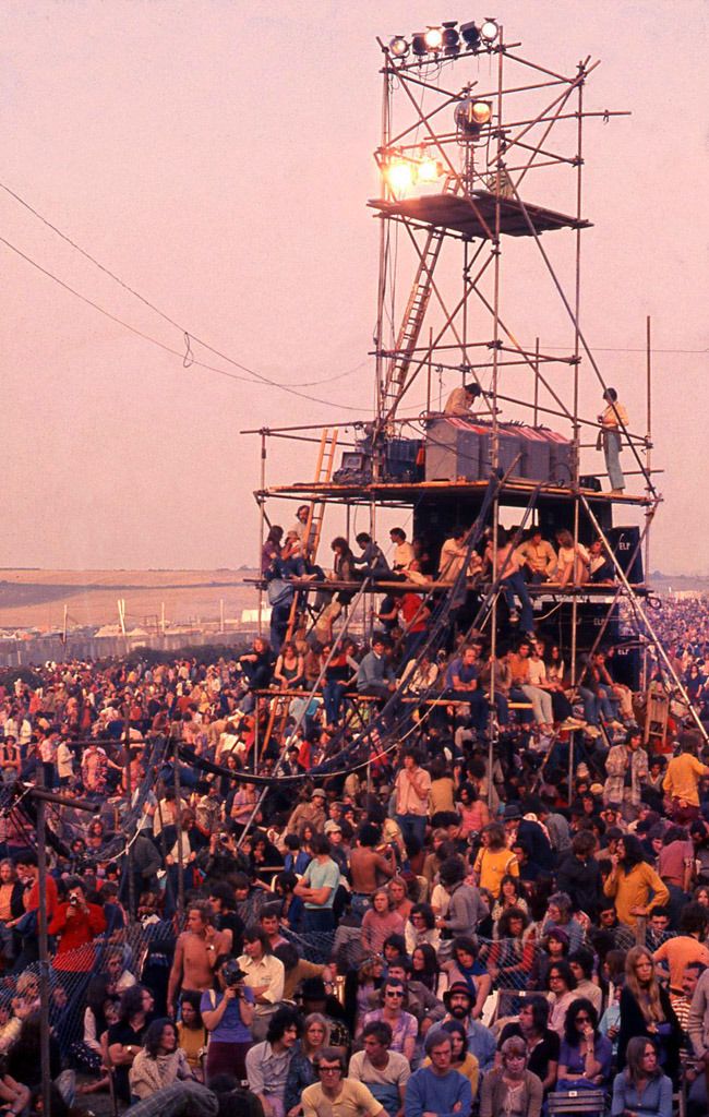 a large group of people sitting on top of a scaffolding structure in the middle of a field