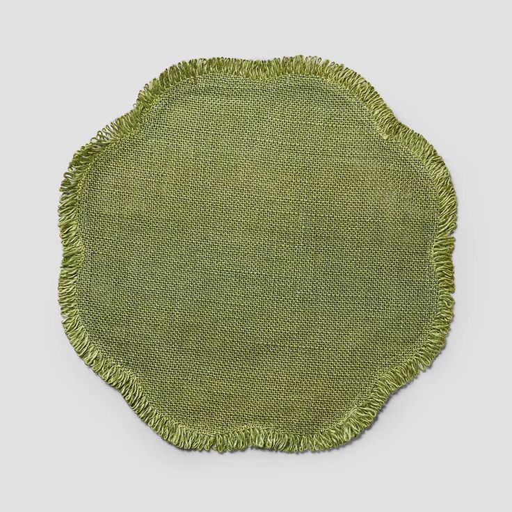 a round green rug with fringes on the edges and bottom, in front of a gray background