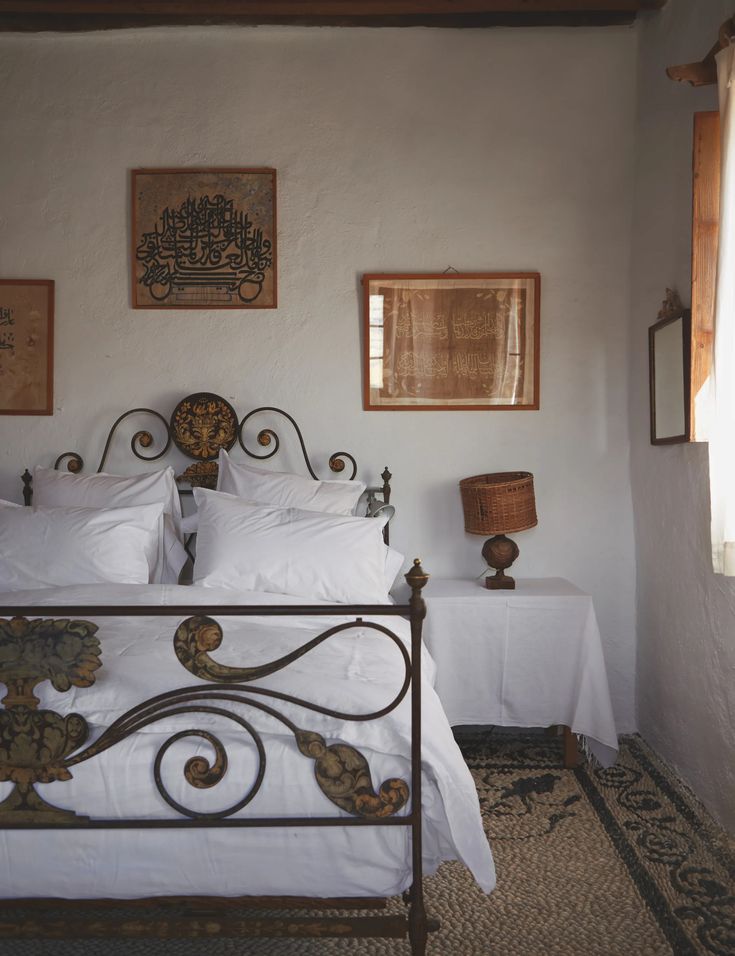 a bed with white sheets and pillows in a bedroom next to two pictures on the wall