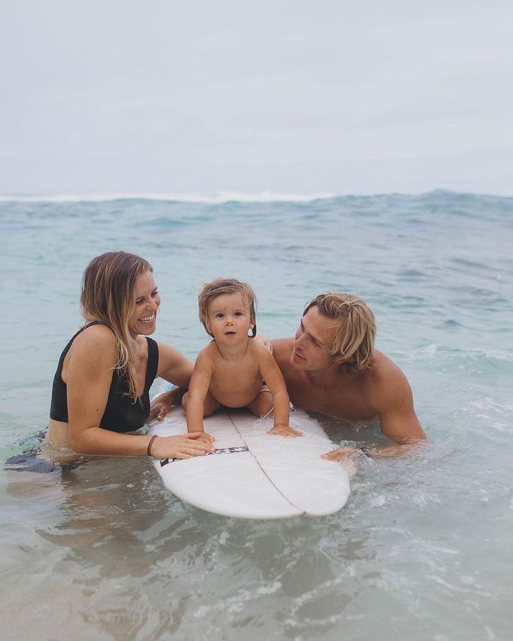 a man, woman and child are in the water with a surfboard on their stomach