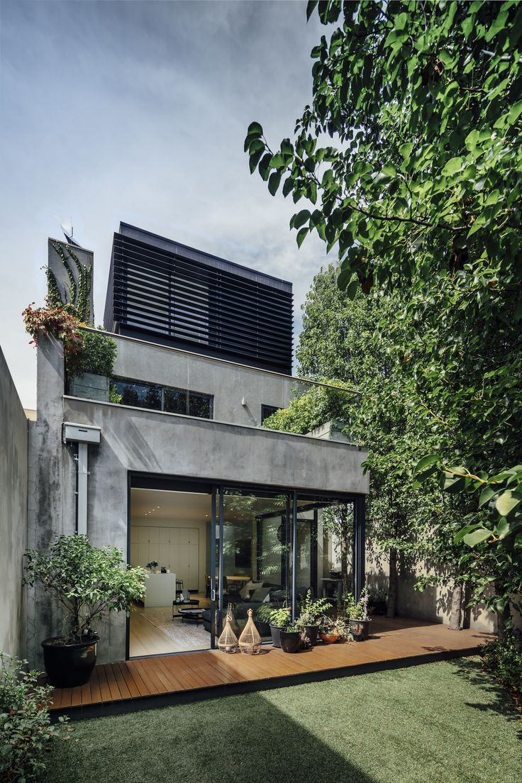 a modern house with wooden decking and green plants on the outside, surrounded by greenery