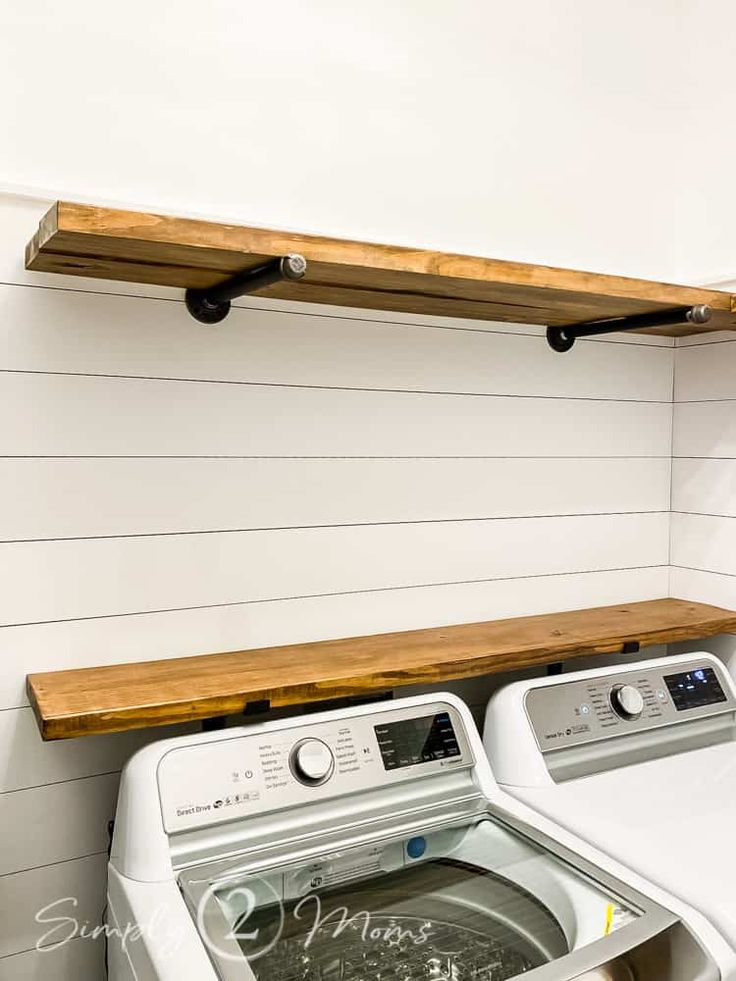 a washer and dryer in a white laundry room with wood shelves above them