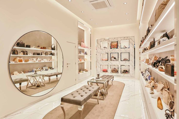 the inside of a shoe store with many shoes on shelves and a bench in front of a large round mirror