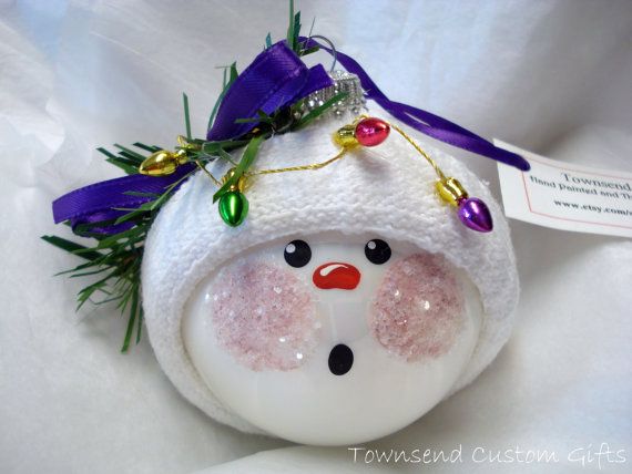 a white snowman ornament with purple ribbon around it's head and eyes