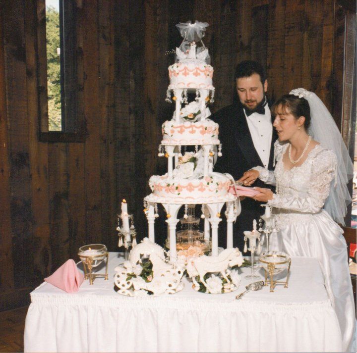 a bride and groom standing next to a wedding cake on a table in front of a wooden wall