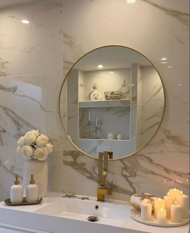 a bathroom sink with candles and flowers on the counter next to it, in front of a round mirror