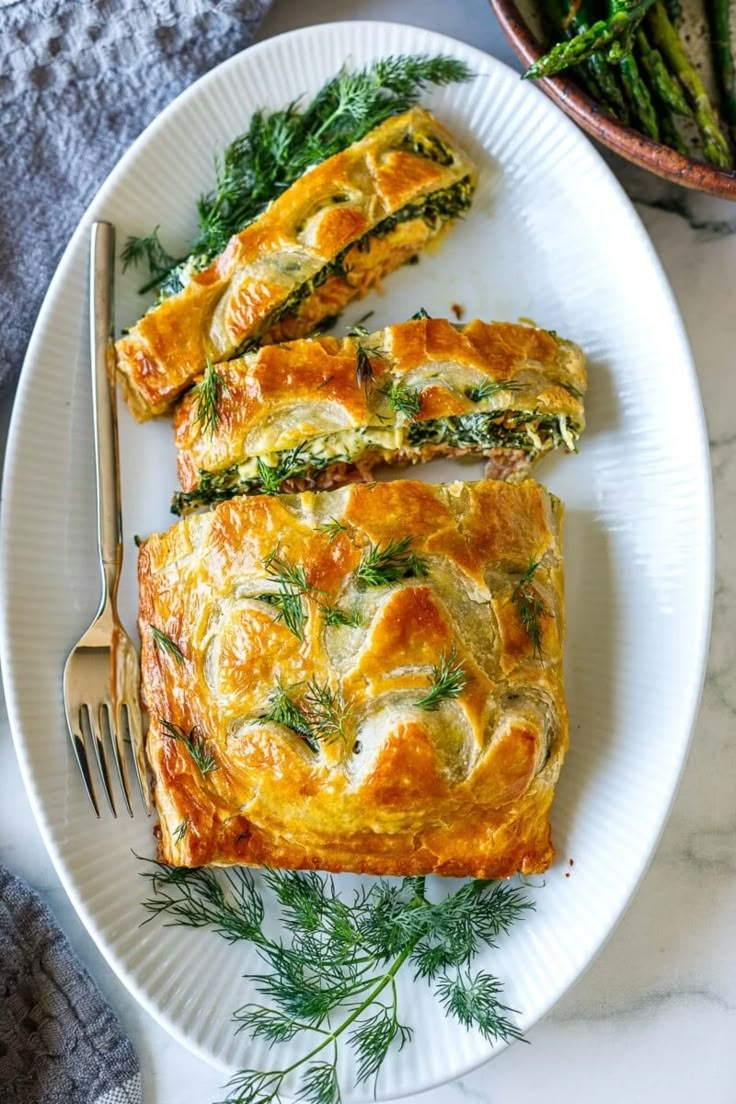 a white plate topped with an omelet next to a bowl of asparagus