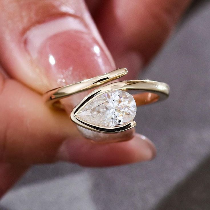 a close up of a person holding a ring with a pear shaped diamond in it