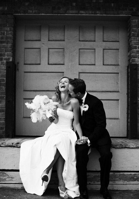 a bride and groom are sitting on the steps outside their wedding venue in black and white