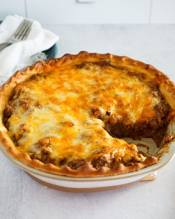 a cheesy dish on a table with a fork and knife next to it