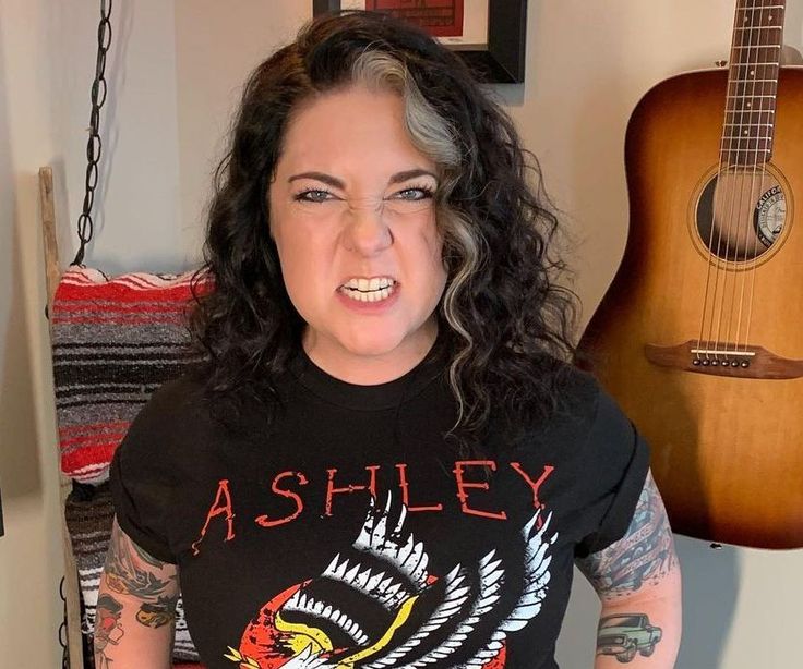 a woman with long hair wearing a black t - shirt and holding an acoustic guitar