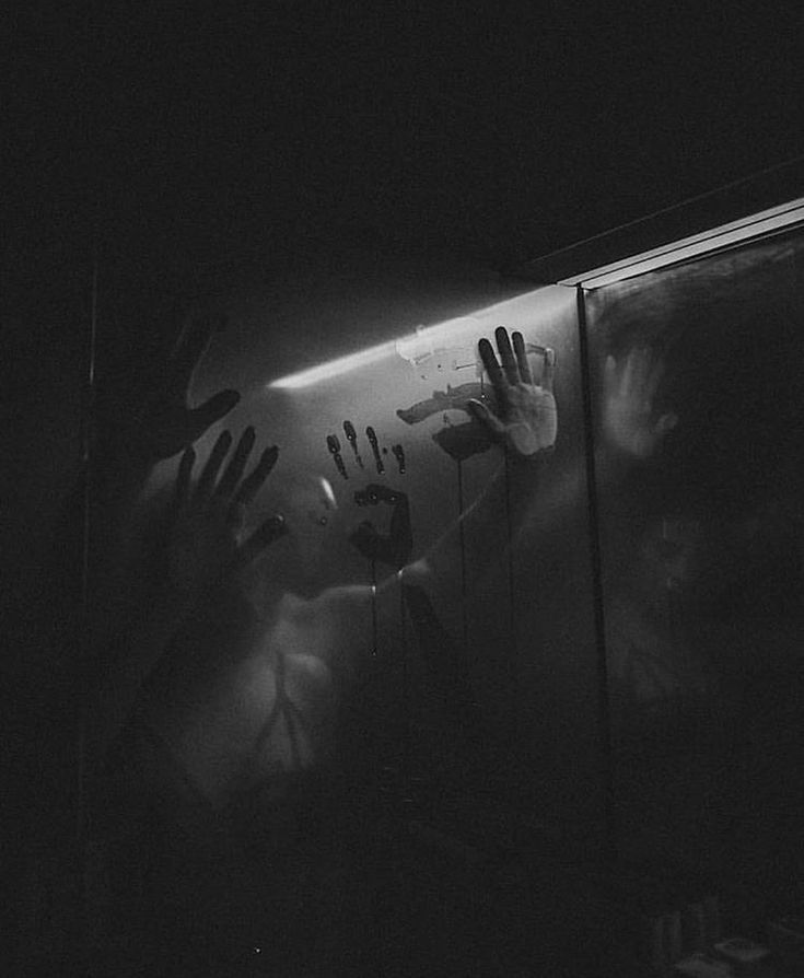 a black and white photo of two hands reaching out from behind a glass door in the dark