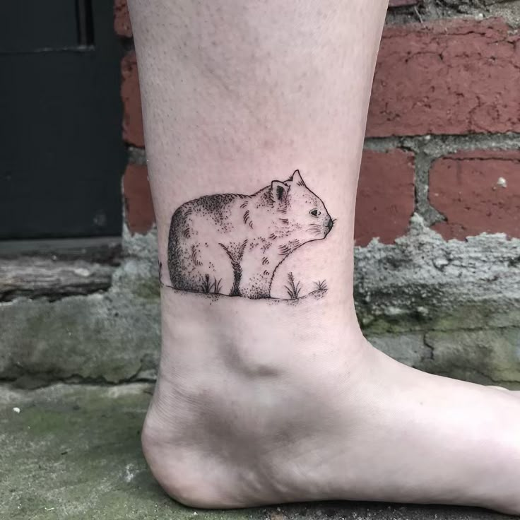 a small bear tattoo on the ankle is shown in black and grey ink, with an animal