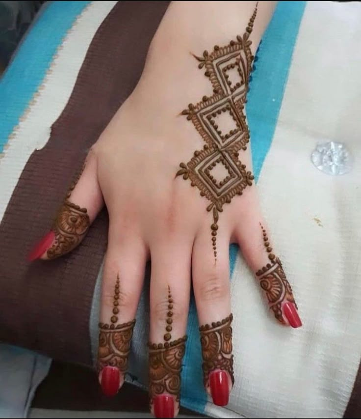 a woman's hand with henna tattoos on her left arm and red nails