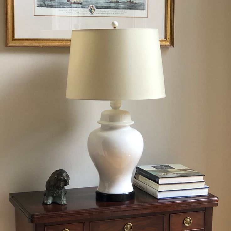 a white lamp sitting on top of a wooden table next to a book case and a dog figurine