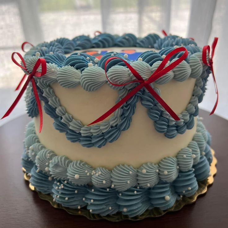 a cake with blue icing and red ribbon on top sitting on a wooden table