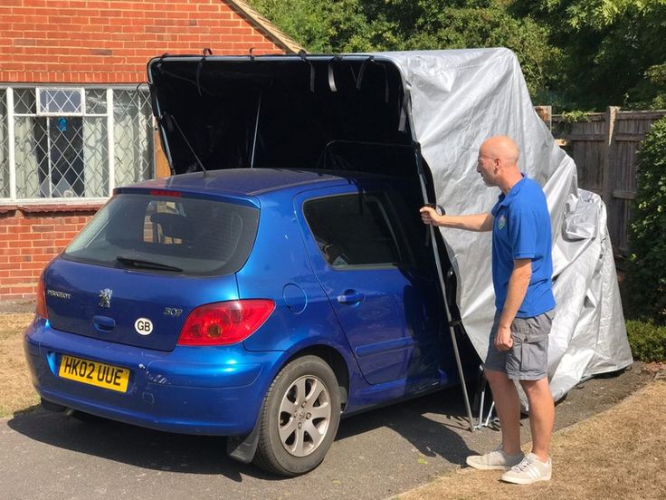 a man standing next to a blue car in front of a house with a tarp over it