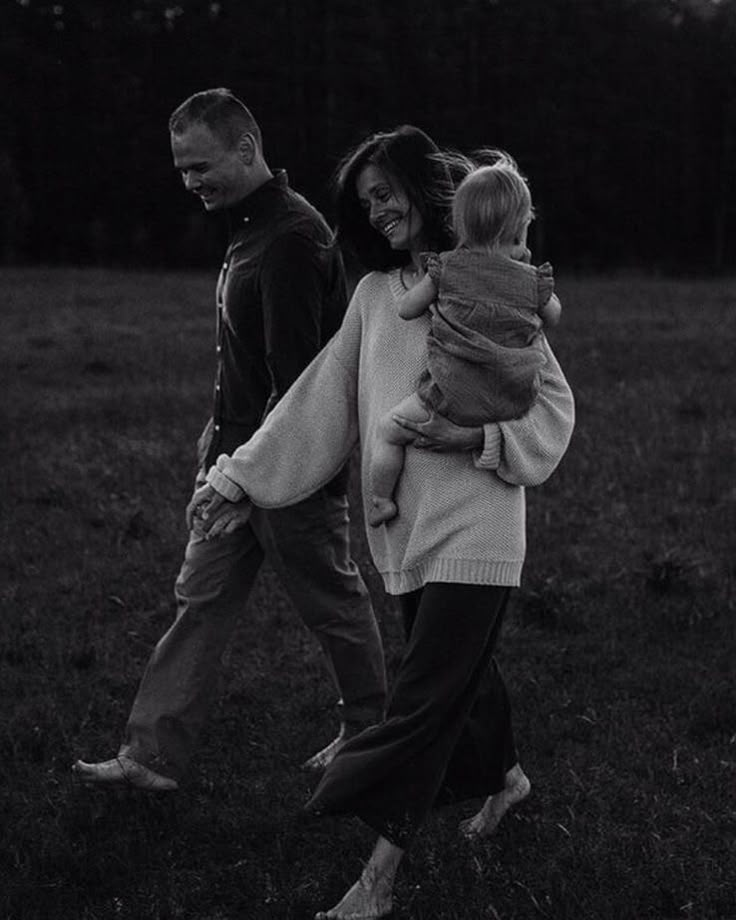 a man and woman walking through a field with a child on their back, in black and white