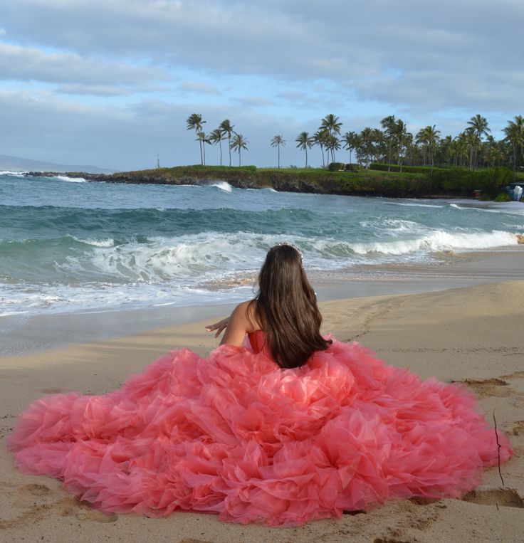 a woman in a pink dress is sitting on the beach and looking at the ocean