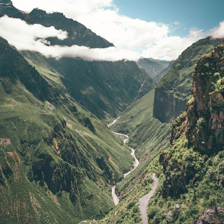 a view of a valley with mountains in the background and clouds hovering over the valleys