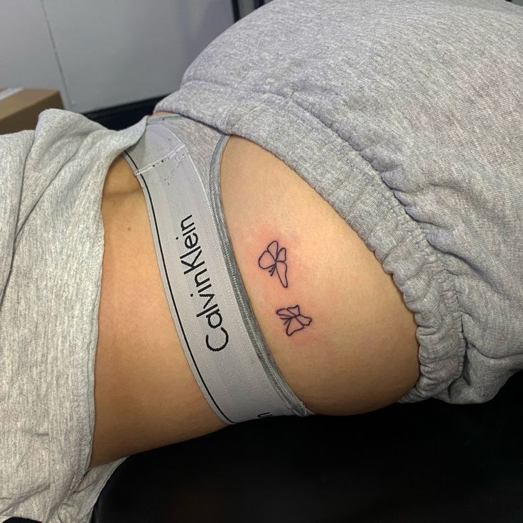 a woman's lower back with a bow tattoo on her left side