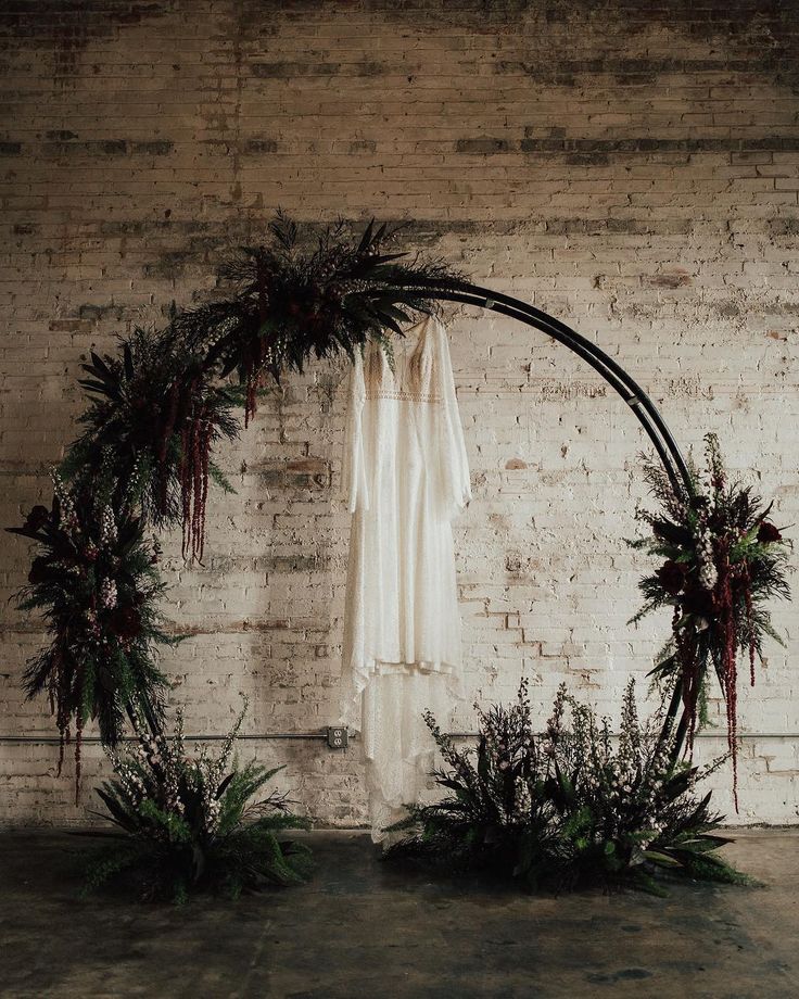 a wedding arch decorated with greenery and hanging ribbons in front of a brick wall