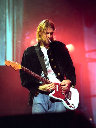 a man with long hair playing an electric guitar in front of a red stage light