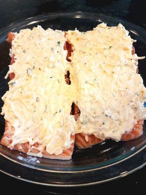 two slices of salmon covered in cheese on a glass plate with a black table top