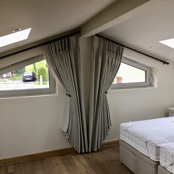 a bed sitting under two windows next to a window sill with curtains on it